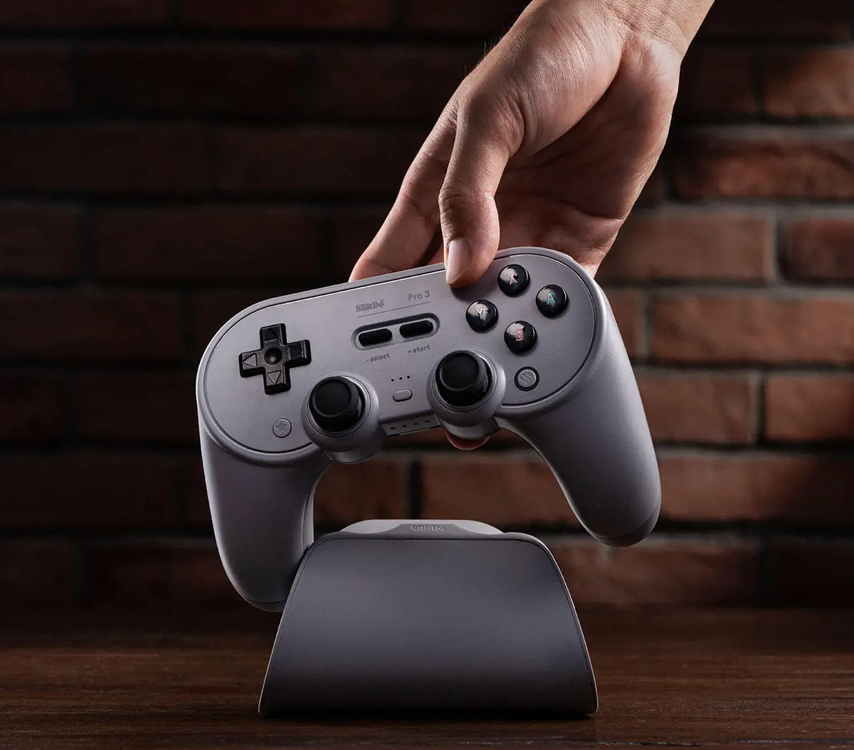 Hand lifting a gray 8BitDo Pro 3 controller off its charging dock