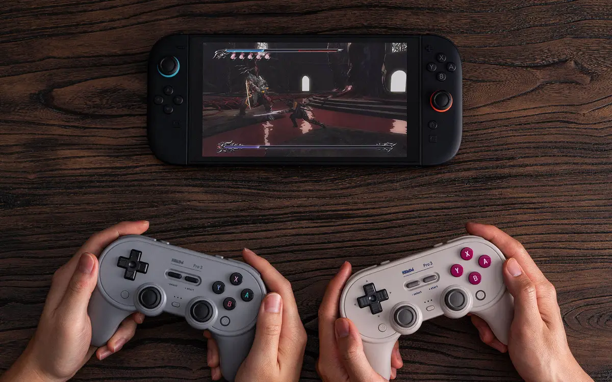 Two hands holding gray and cream Pro 3 controllers in front of a handheld console