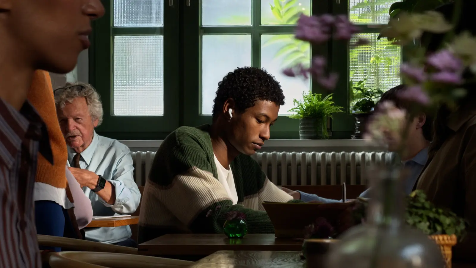 Person wearing Apple AirPods 5 while reading in a cafe