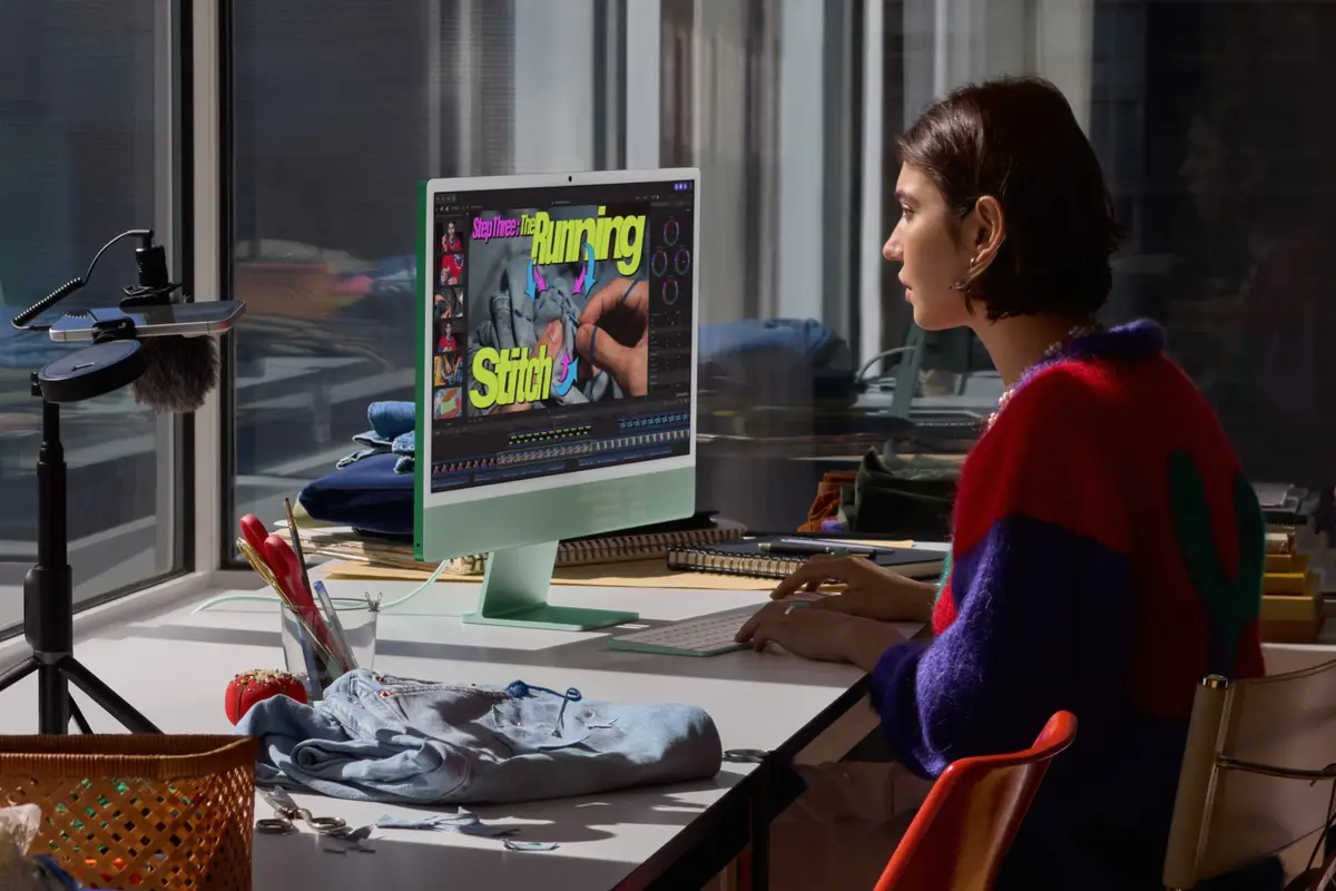 A person editing video on a green 24-inch iMac at a desk