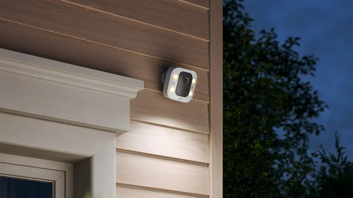 Blink Spotlight Cam 2K+ mounted on a house wall at night with its lights on