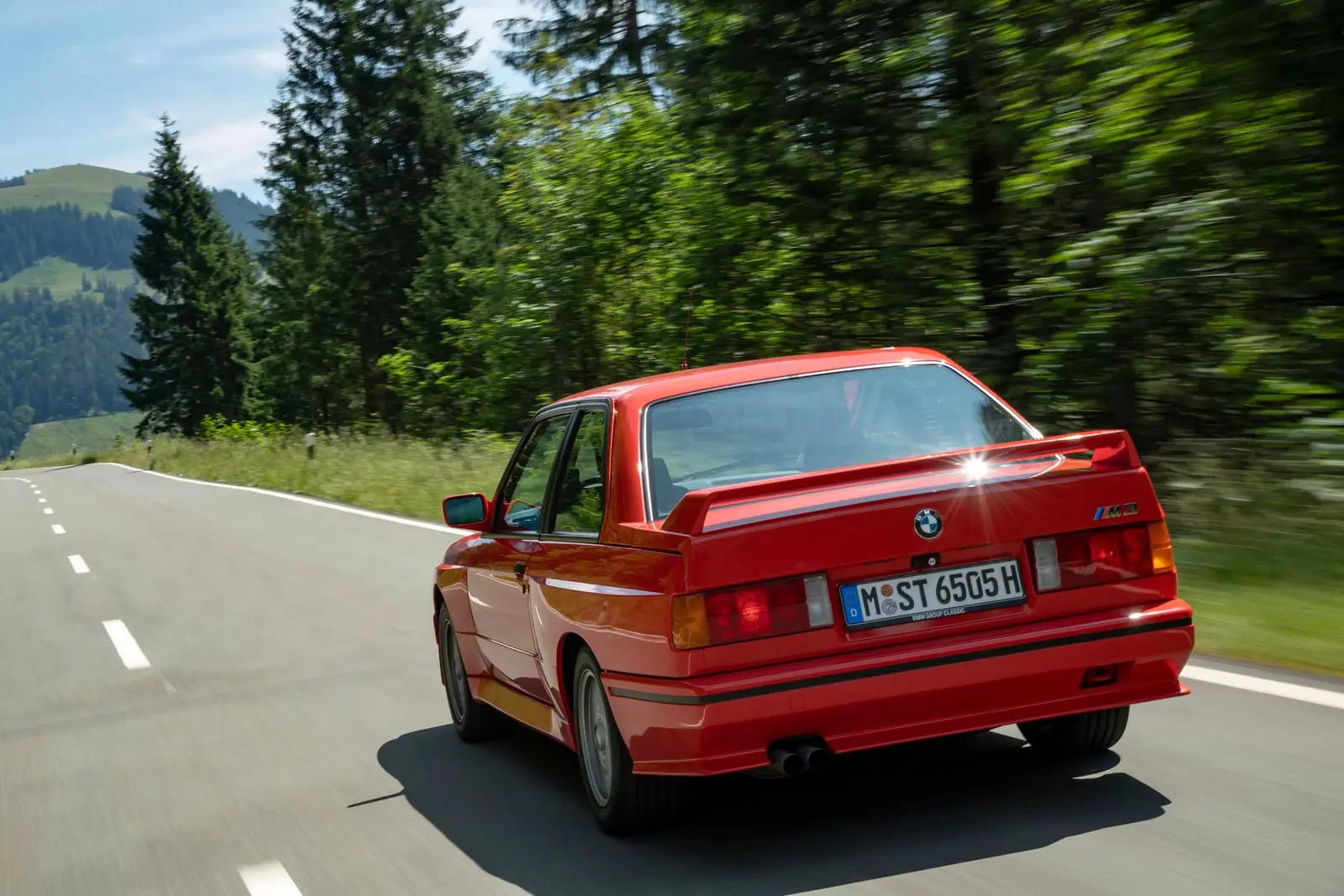 Red first generation BMW M3 driving on a country road