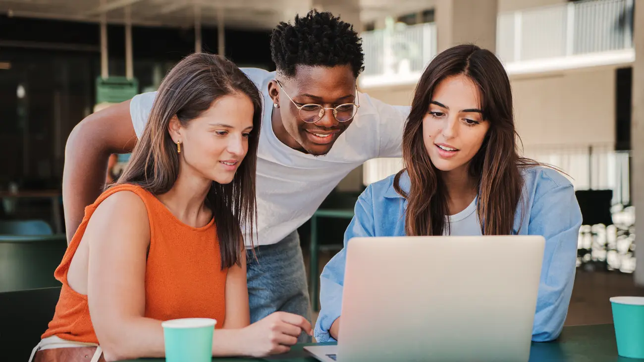 Three college students looking at a laptop together at a campus table