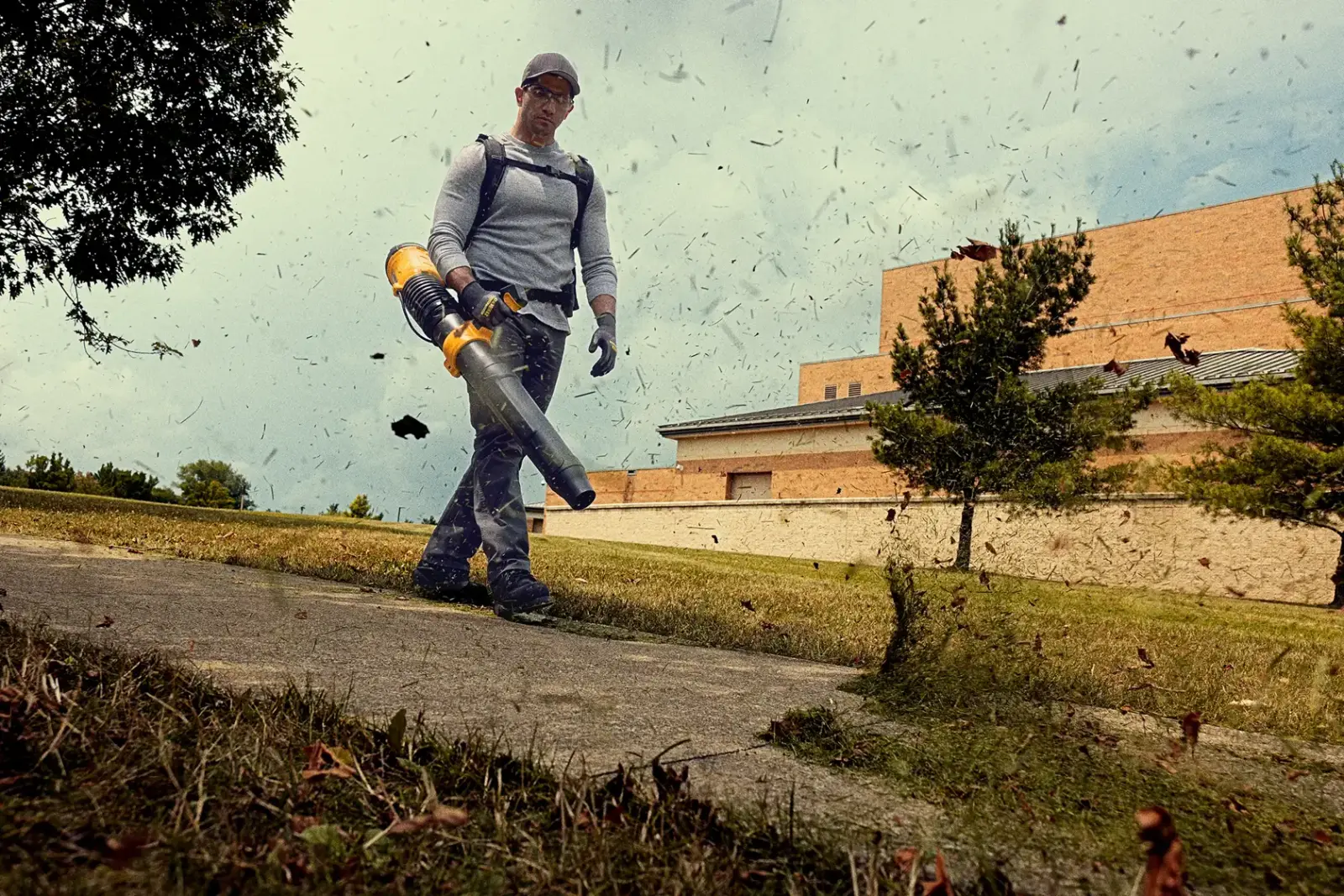 DeWalt 60V MAX 백팩 블로워로 길 위의 낙엽을 치우는 작업자