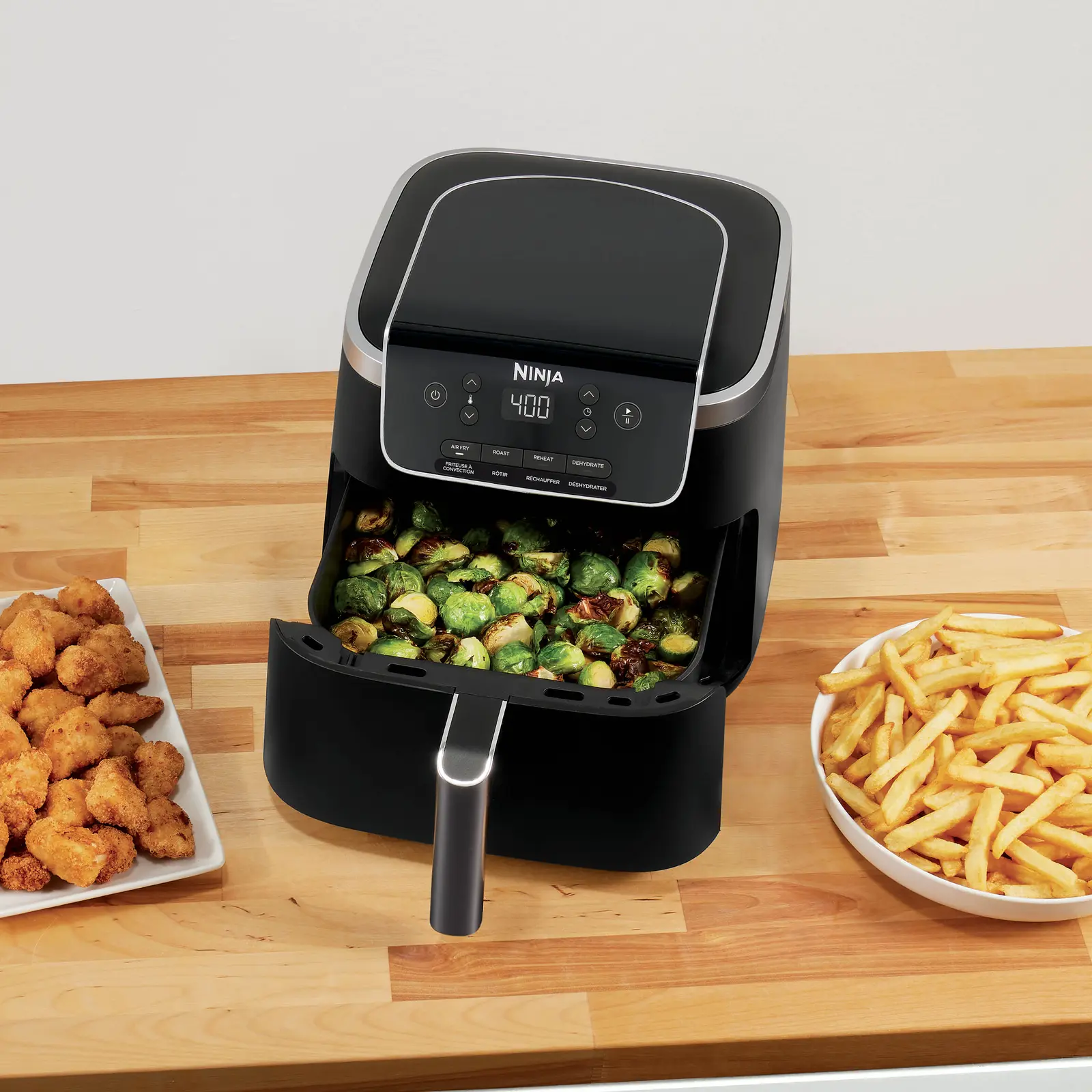 Ninja Air Fryer Pro 4-in-1 with roasted Brussels sprouts in the basket beside plates of nuggets and fries