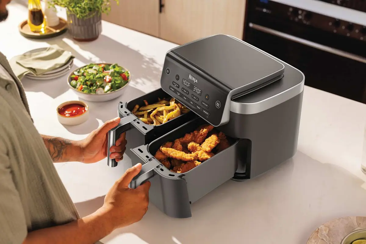 Person lifting a basket out of the Ninja DualZone air fryer on a kitchen counter