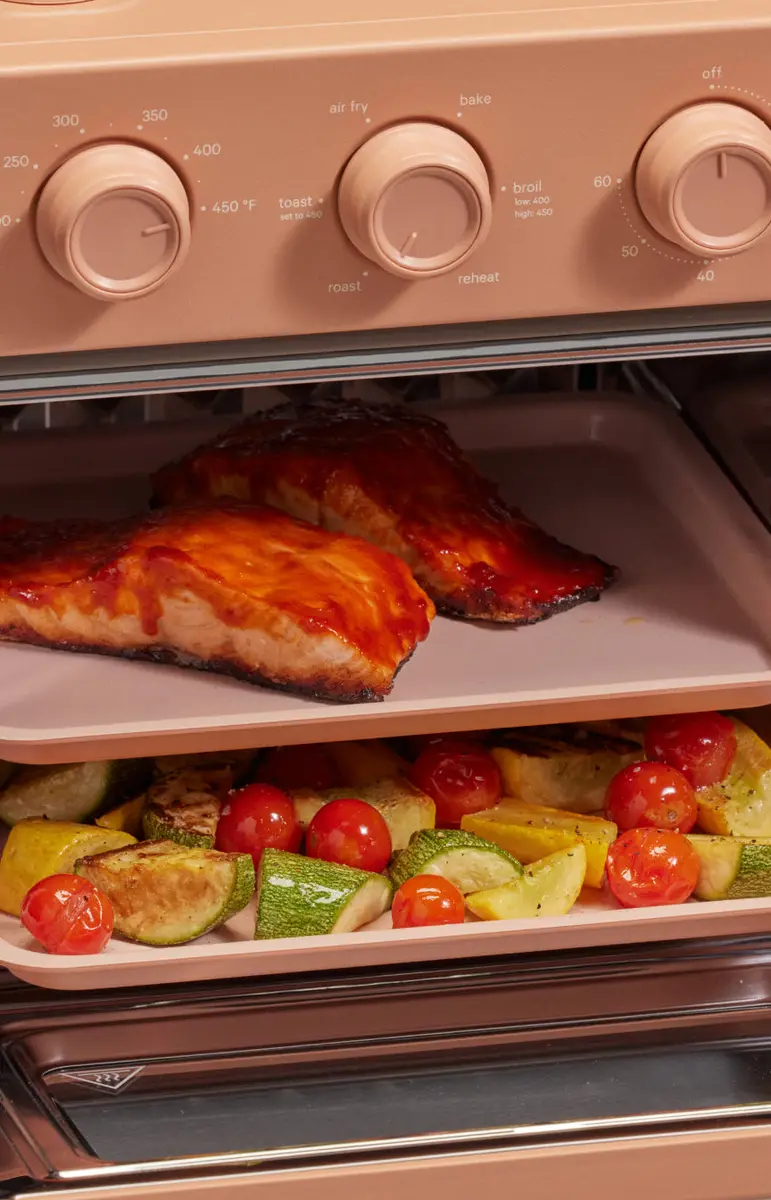 Salmon fillets and a tray of roasted vegetables cooking in a pink Wonder Oven