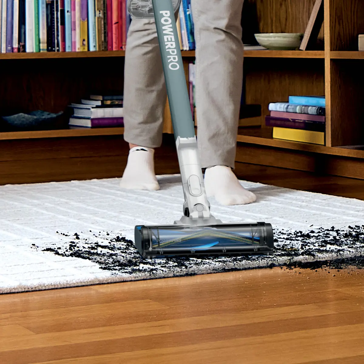 Vacuum head picking up debris from a white rug next to a wood floor