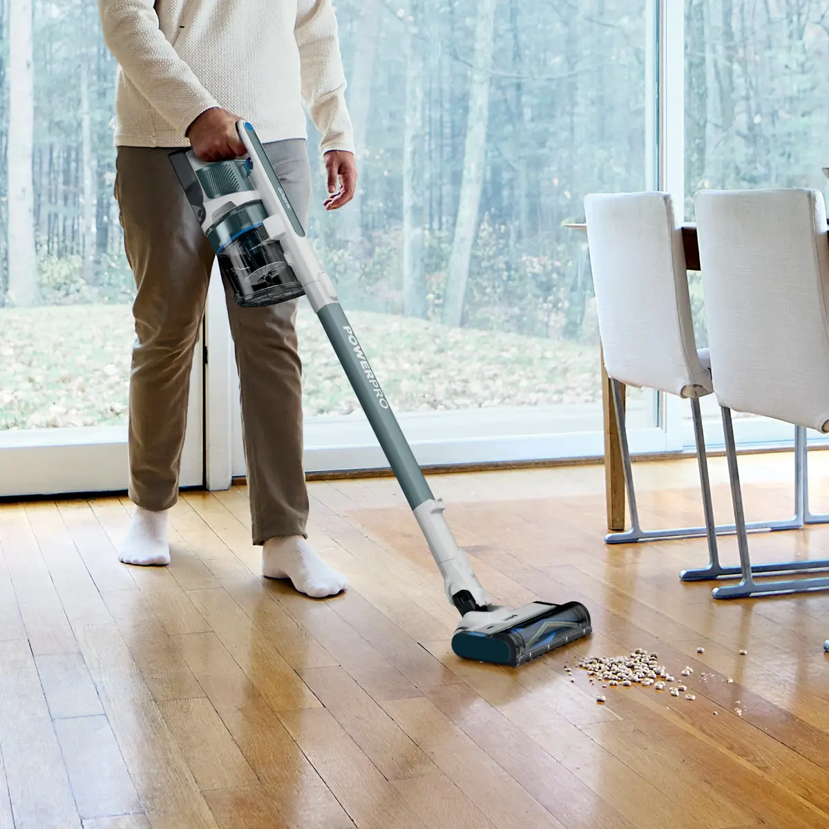 Person using the vacuum on a hardwood floor near a dining table