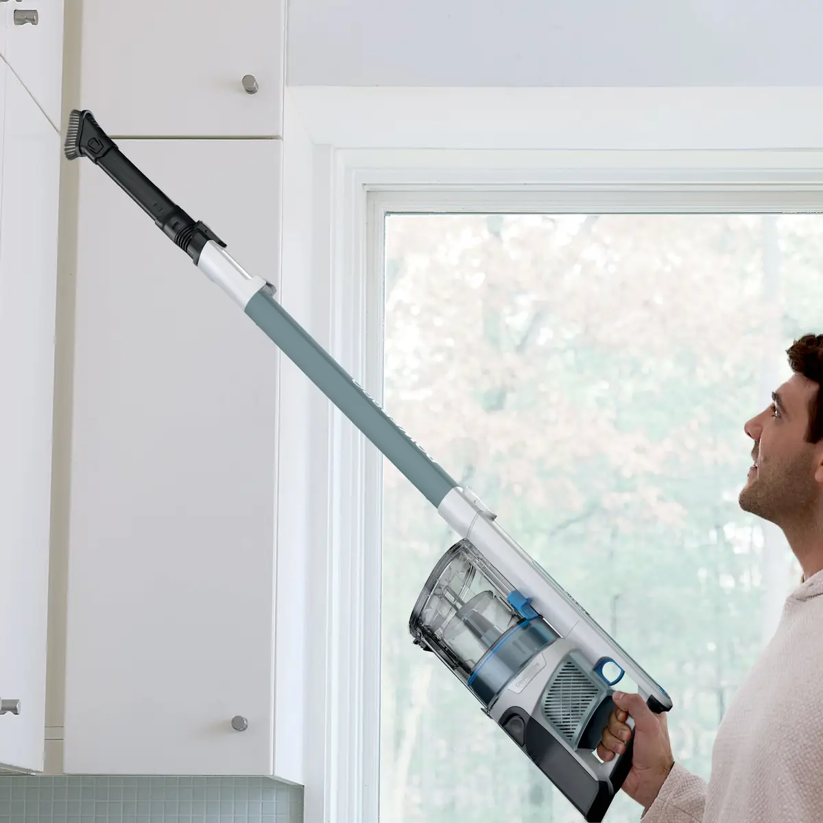 Man using the vacuum as a handheld with a long wand to clean high shelves