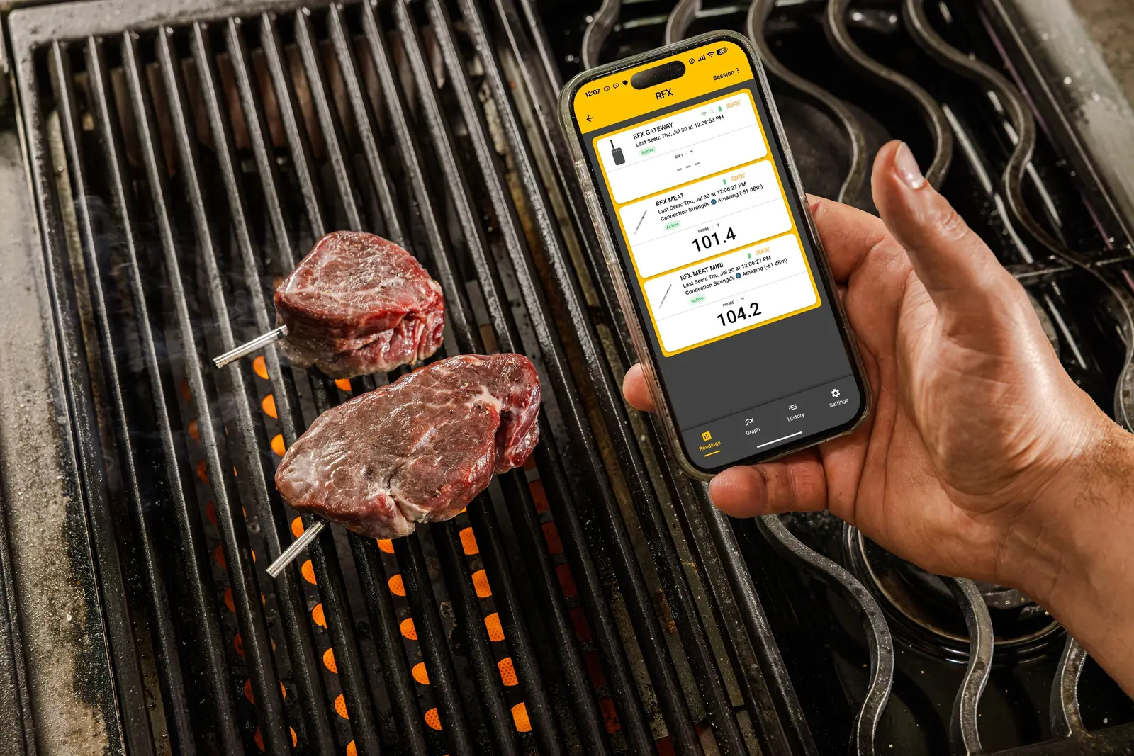 그릴 위 필레 스테이크 두 점에 꽂힌 ThermoWorks RFX MEAT Mini 프로브와 RFX 앱이 열린 스마트폰